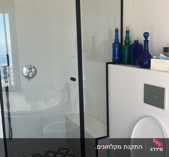 מקלחון זכוכית פינתי מותקן עם פרופילים שחורים בחדר רחצה